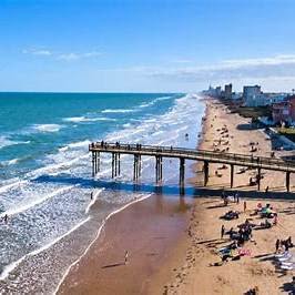 Sunny beach with pier and ocean waves.